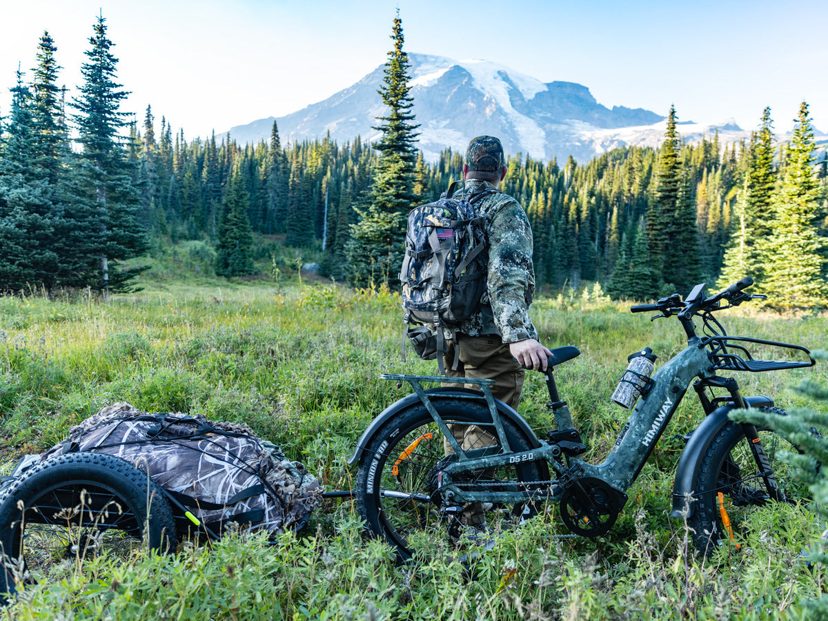 Himiway D5 2.0 Camo e-bike with a gear trailer in a mountain meadow