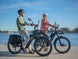Two riders on Himiway A7 e-bikes along a waterfront path